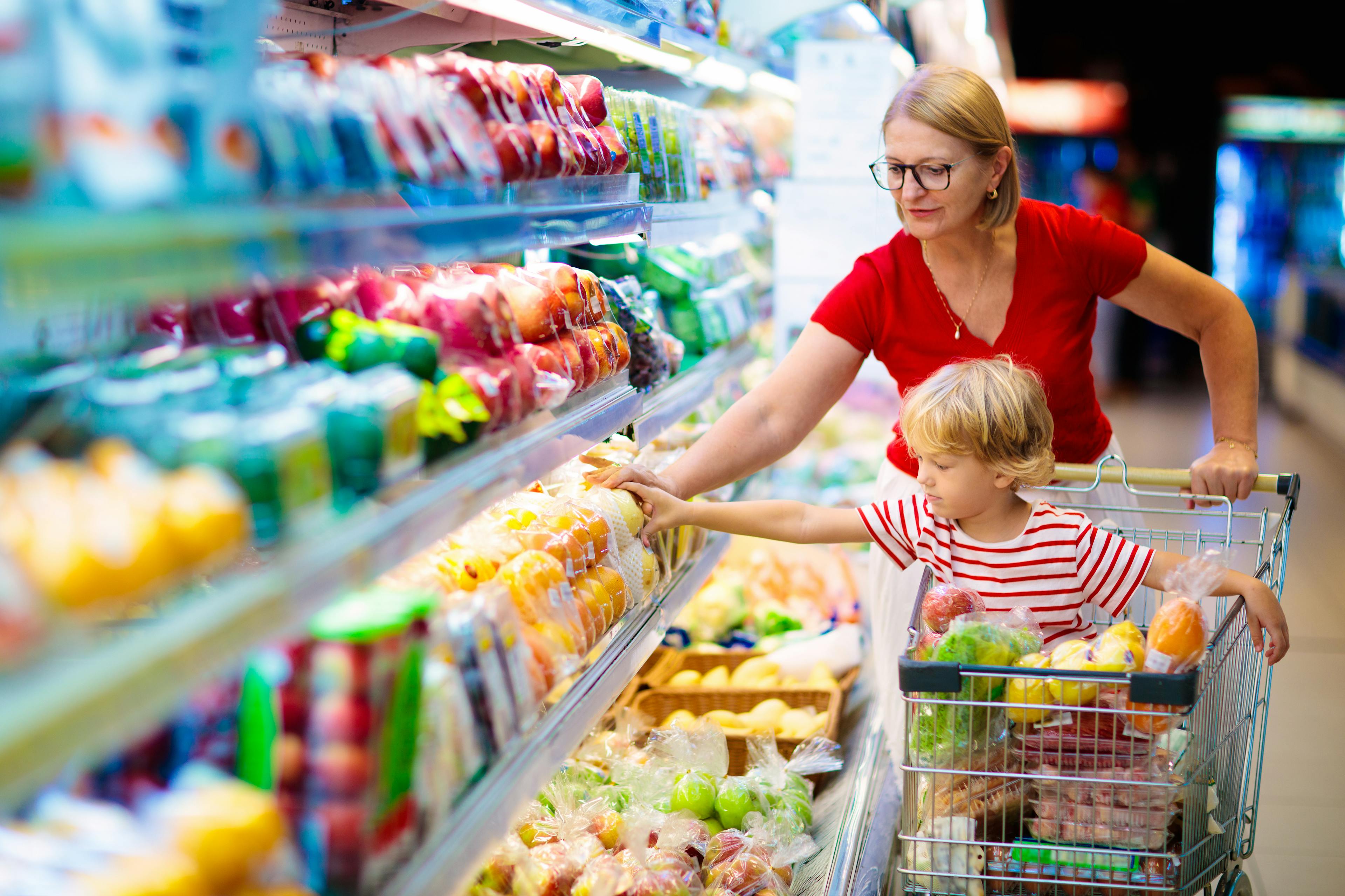 a woman pushing a child in a shopping trolley in a grocery store aisle